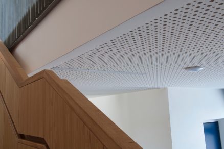 Detail kulatého děrování z interiéru dobřichovické školy. Instalace na stropním podhledu dokáže výrazně utlumit hluk vznikající volným pohybem žáků na chodbách