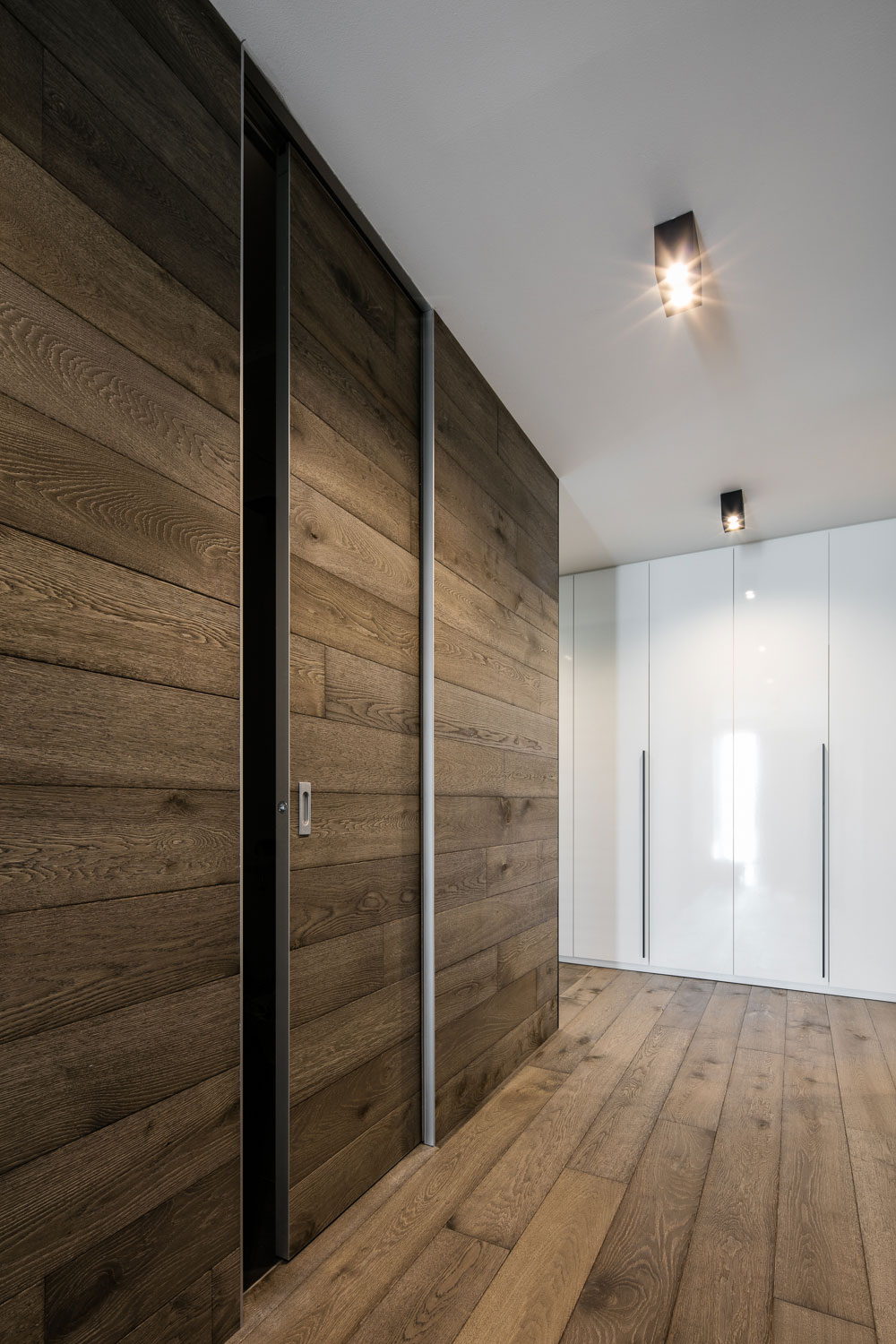 Shodná dřevěná dýha se prolíná na podlaze stěně i na dveřích MASTER DOOR sahajících od podlahy až ke stropu ve stavebním pouzdře AKTIVE.