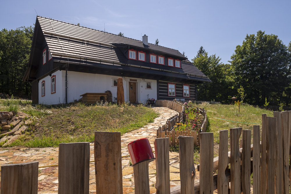 K návštěvě zve příchozí vydlážděný úhledný chodník roubenku přesněji poloroubenku hlídá při vstupu děd Krušnohor.