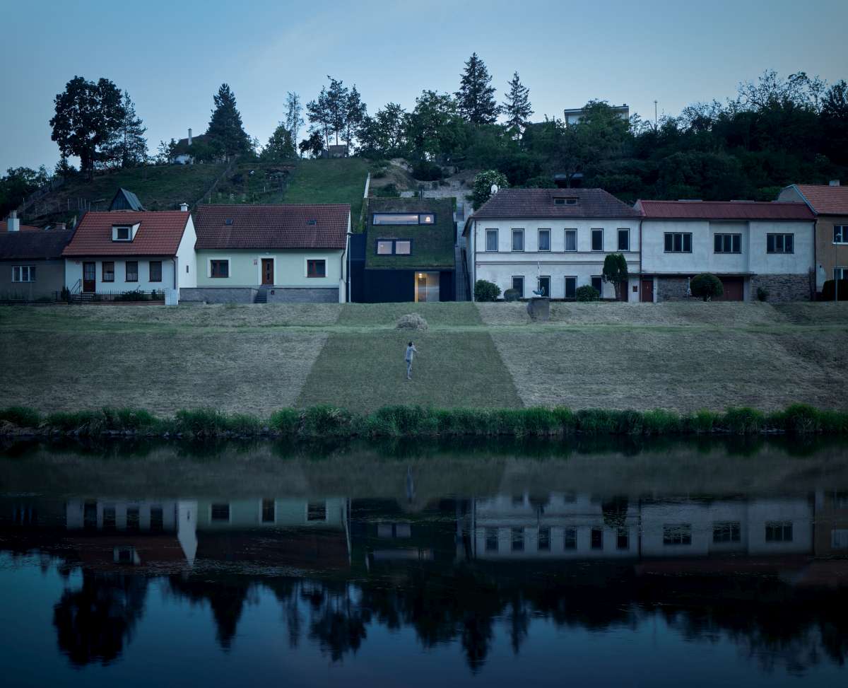 Rodinný dům na nábřeží se zelenou střechou.