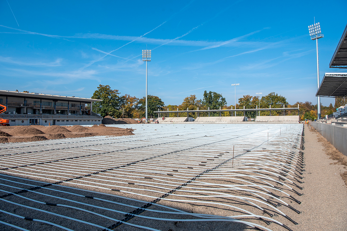  Instalace vyhřívacího systému REHAU na fotbalovém stadionu v Pardubicích, zachycující pokládku potrubí pro rovnoměrné vytápění trávníku.