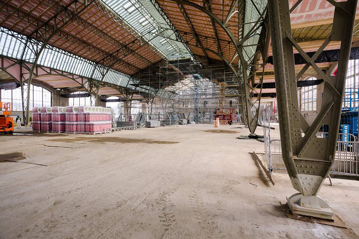 Rozsáhlý interiér střední haly s montážním materiálem a nosnou ocelovou konstrukcí během rekonstrukce.