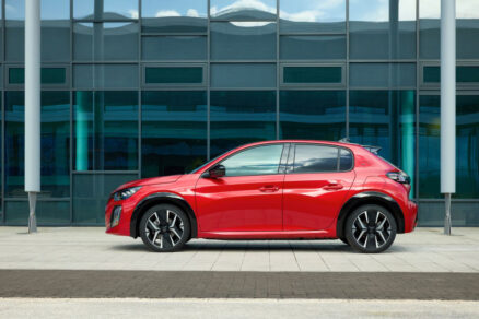 Boční pohled na Peugeot E-208 před moderní budovou