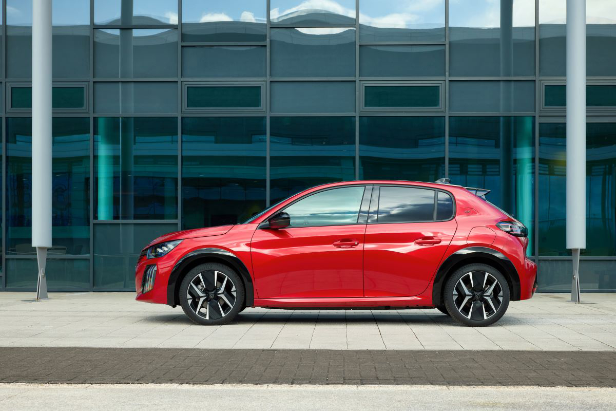 Boční pohled na Peugeot E-208 před moderní budovou