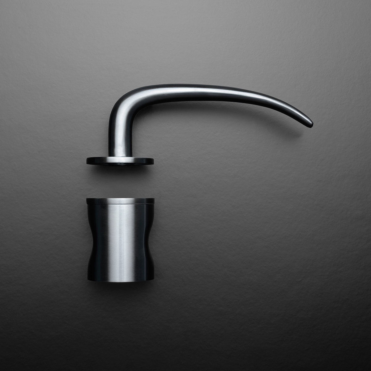 Detailní pohled na moderní designovou kliku z broušené nerezové oceli na tmavém pozadí.