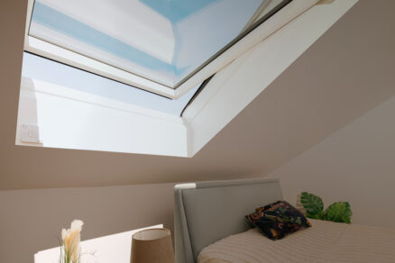 Střešní okno VELUX ve světlé podkrovní ložnici s výhledem na oblohu