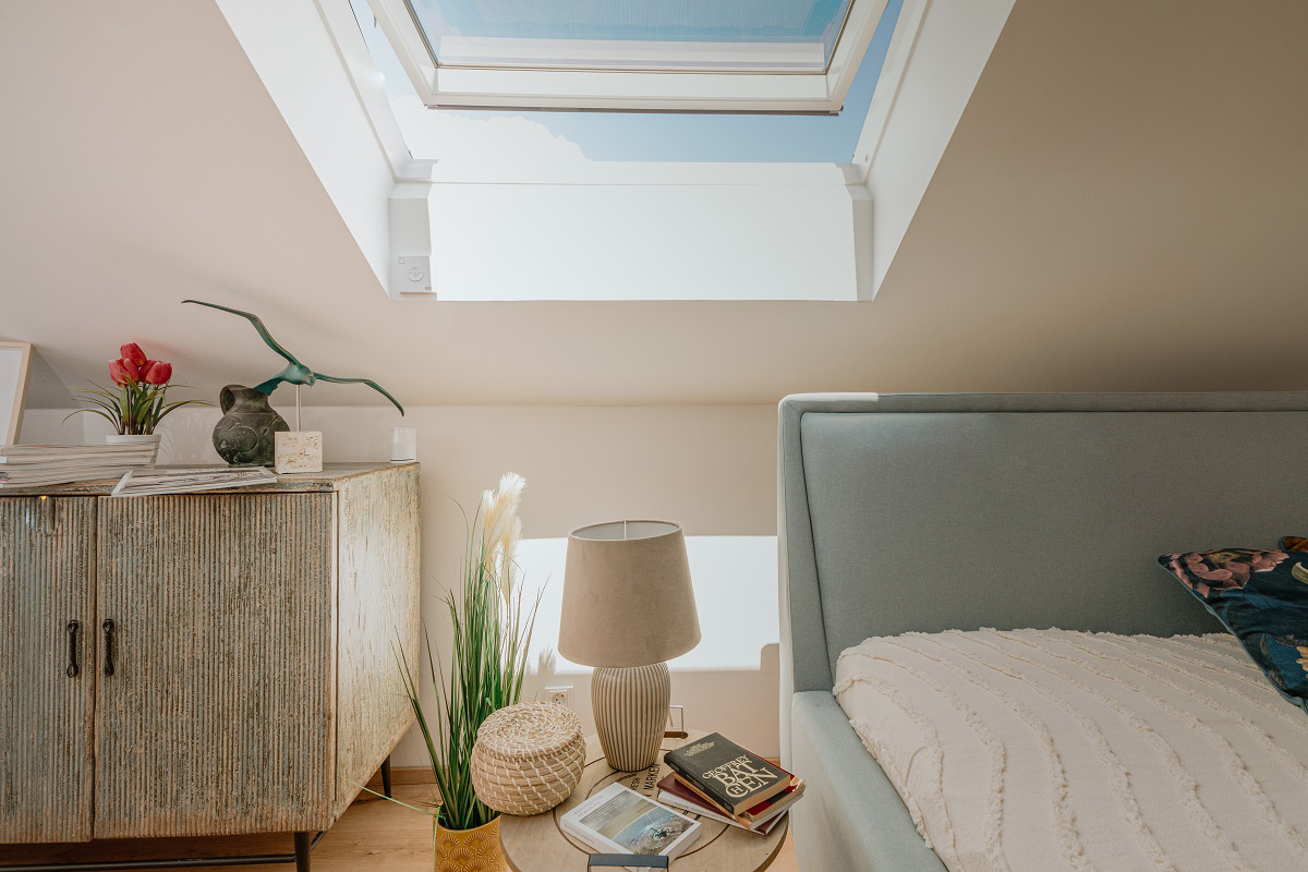 : Ložnice s otevřeným střešním oknem VELUX a výhledem na modrou oblohu