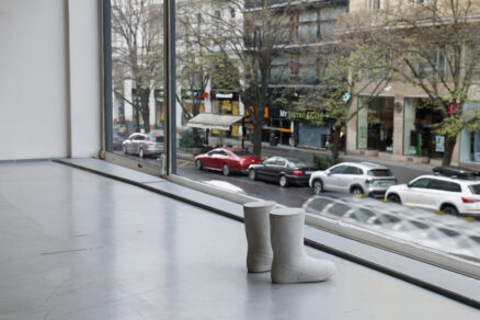 Betonové holínky umístěné u velkého okna s výhledem na městskou ulici