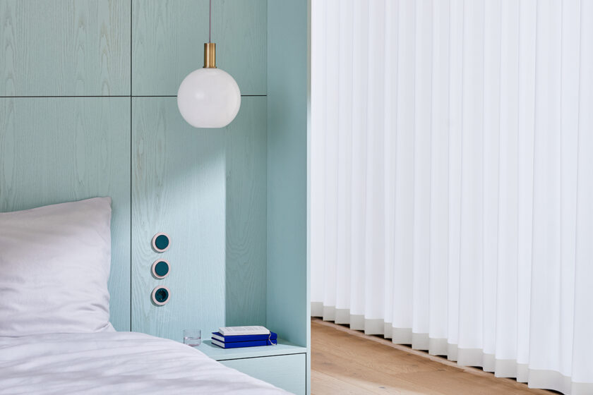 Moderní interiér ložnice s tyrkysovým obložením a designovými vypínači berker integrovánými u postele