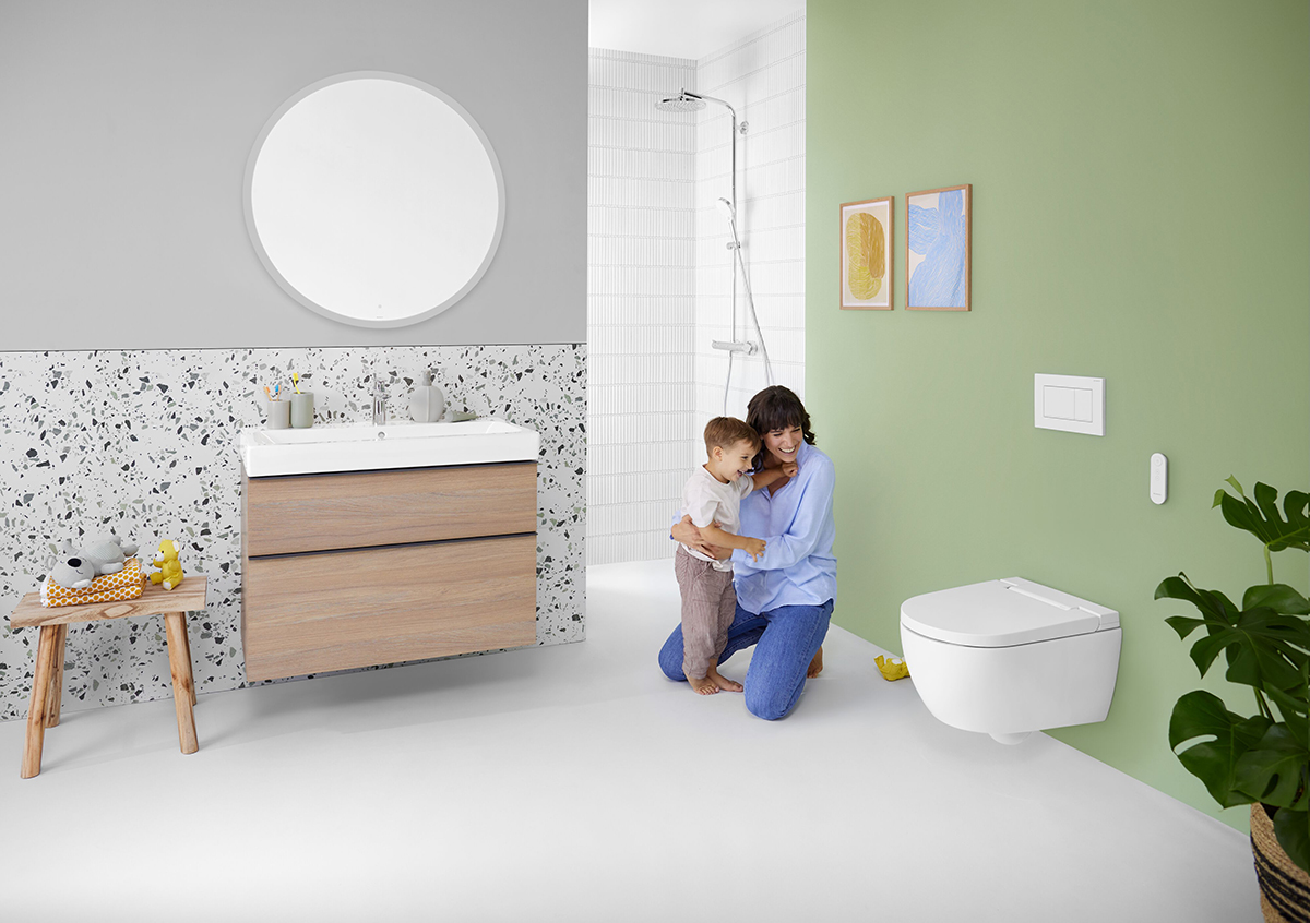 Rodina v koupelně se sprchovacím WC Geberit AquaClean Alba na zelené stěně