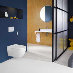 Detailní pohled na sprchovací WC Geberit AquaClean Alba s dálkovým ovládáním na tmavě modré stěně