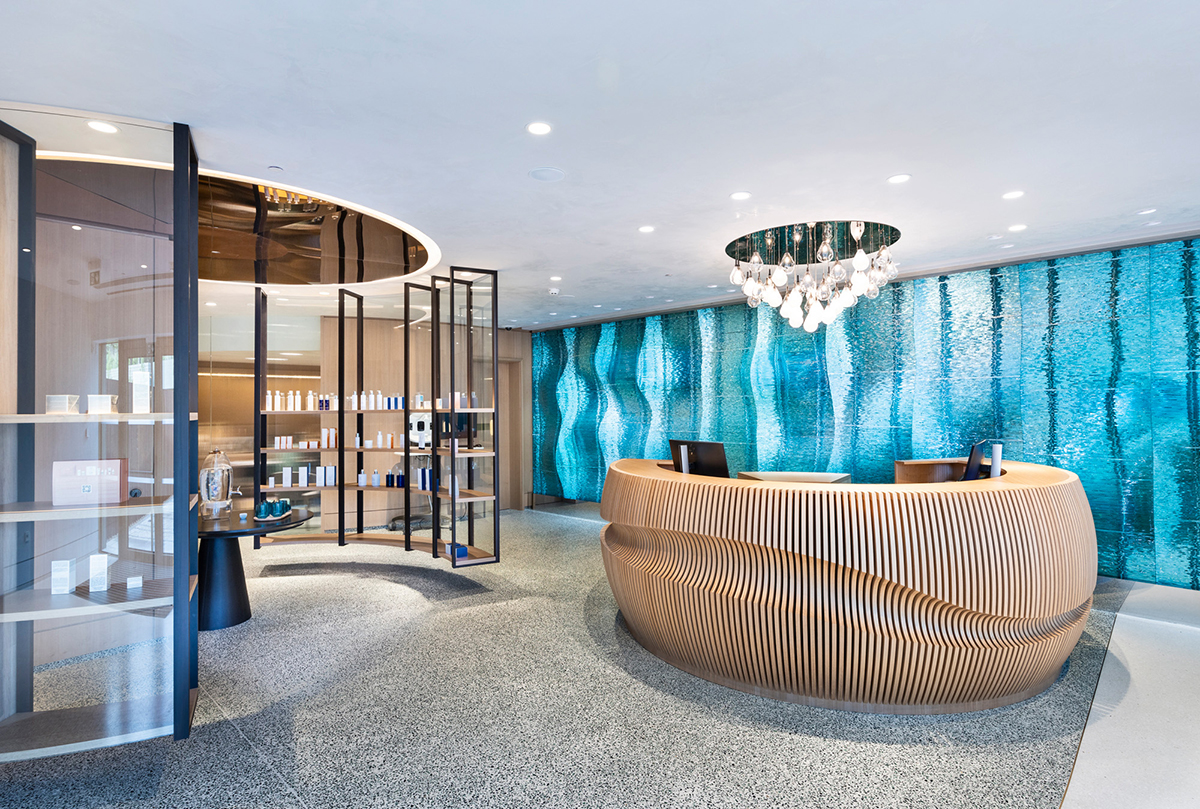 Moderní recepce wellness centra s dřevěným pultem a skleněnou stěnou s vodním motivem