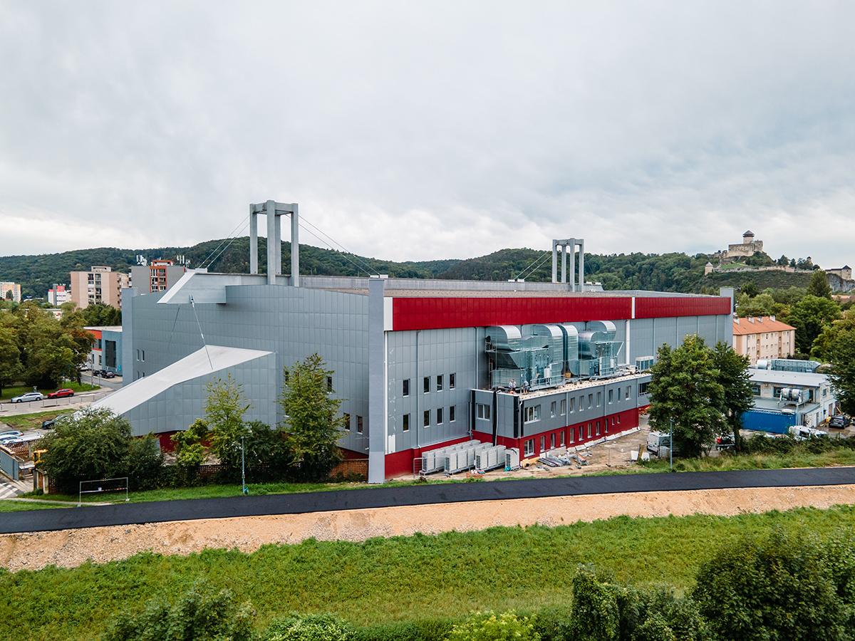 Boční pohled na zimní stadion Pavla Demitry v Trenčíně s výraznými vzduchotechnickými prvky a panoramatem hradu