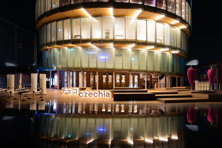 Český pavilon na EXPO 2025 v nočním osvětlení s nasvícenou skleněnou fasádou