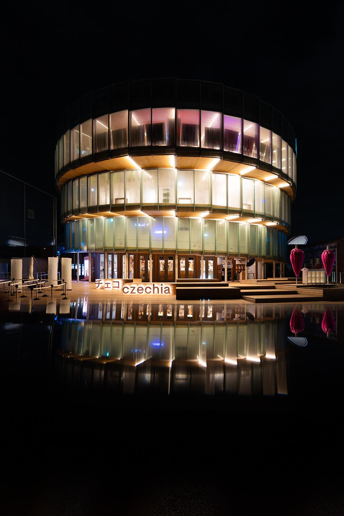 Český pavilon na EXPO 2025 v nočním osvětlení s nasvícenou skleněnou fasádou