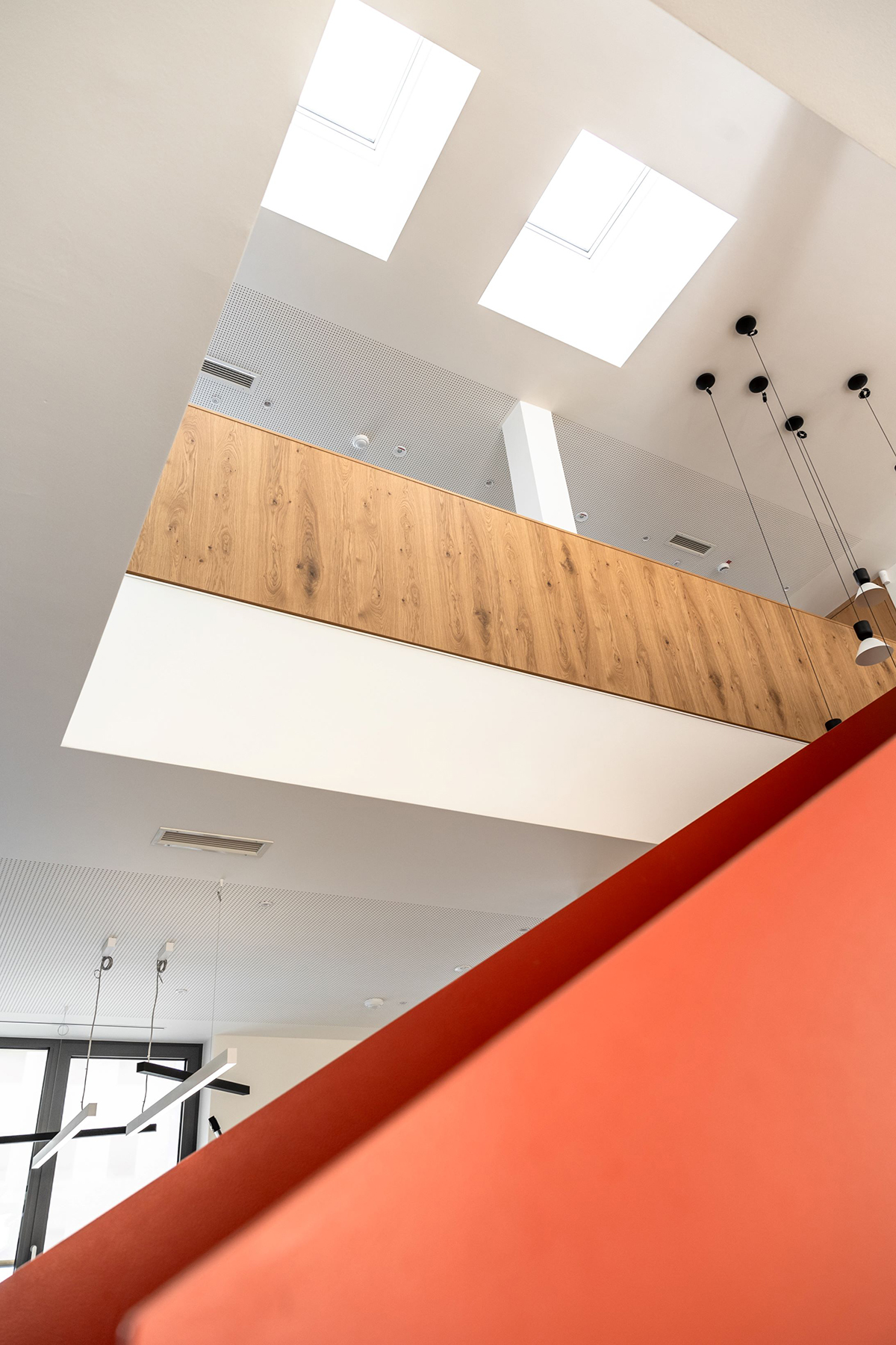 Světlá kancelář s červeným schodištěm a střešními světlíky VELUX.
