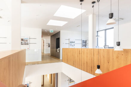 Moderní kanceláře s červeným schodištěm, dřevěným zábradlím a střešními okny VELUX.
