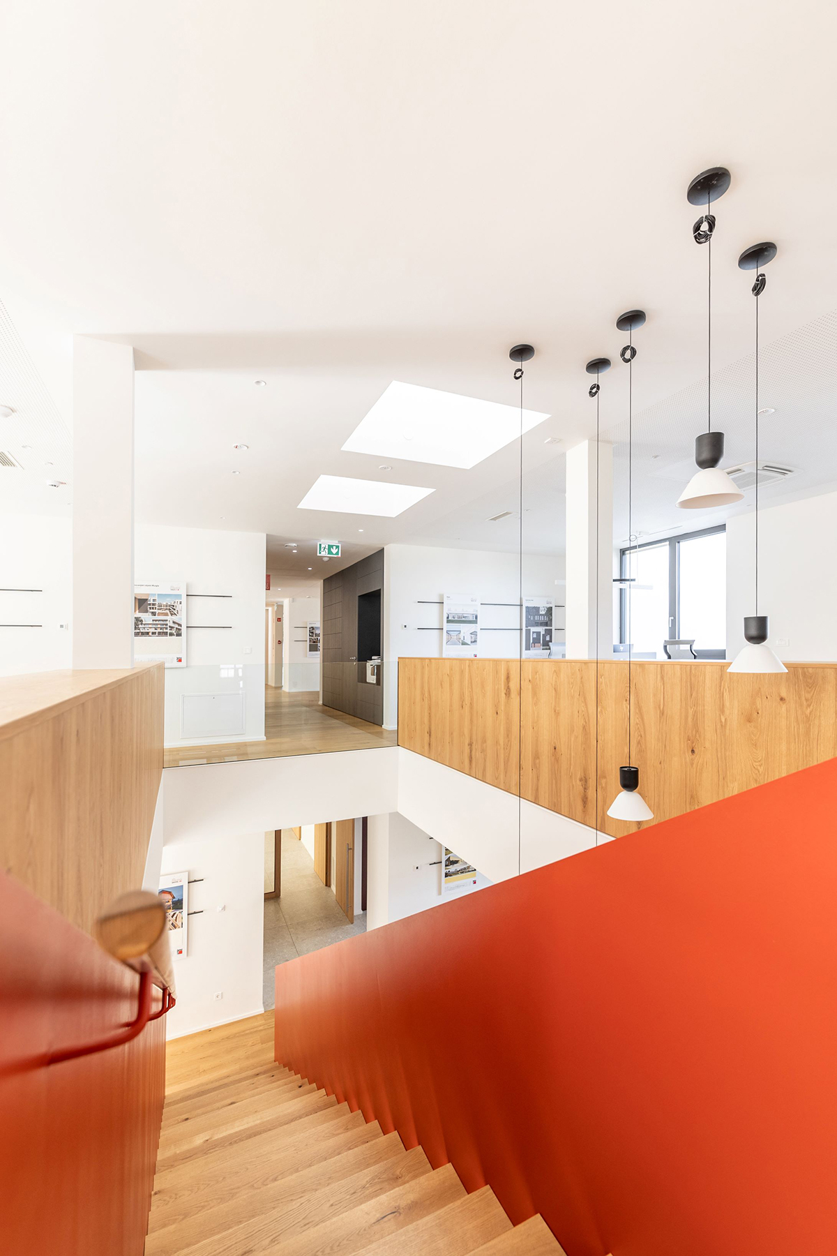 Moderní kanceláře s červeným schodištěm, dřevěným zábradlím a střešními okny VELUX.