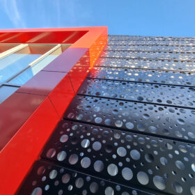 Moderní kovová fasáda z černého děrovaného plechu s výrazným červeným orámováním