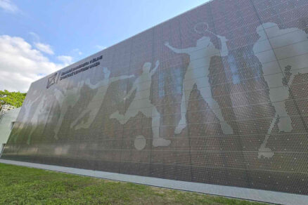 Perforovaná fasáda sportovního centra s motivem sportovců vytvořeným pomocí děrovaného plechu