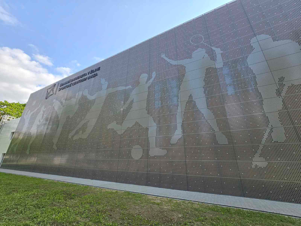Perforovaná fasáda sportovního centra s motivem sportovců vytvořeným pomocí děrovaného plechu