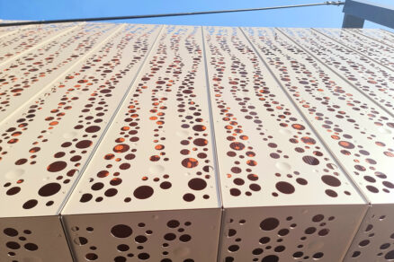 Detail světlé kovové fasády z děrovaných plechů s nepravidelným perforačním vzorem