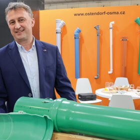 Muž v obleku prezentuje rez plastovým kanalizačním potrubím na výstavním stánku Ostendorf-OSMA