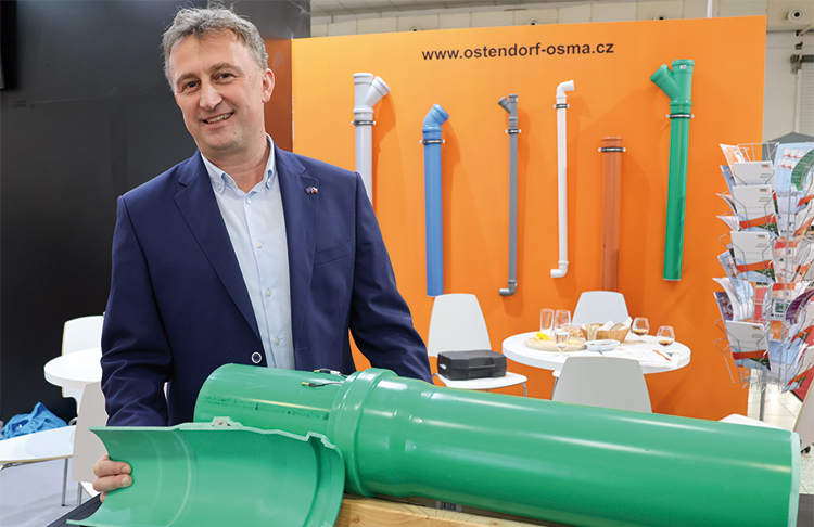 Muž v obleku prezentuje rez plastovým kanalizačním potrubím na výstavním stánku Ostendorf-OSMA