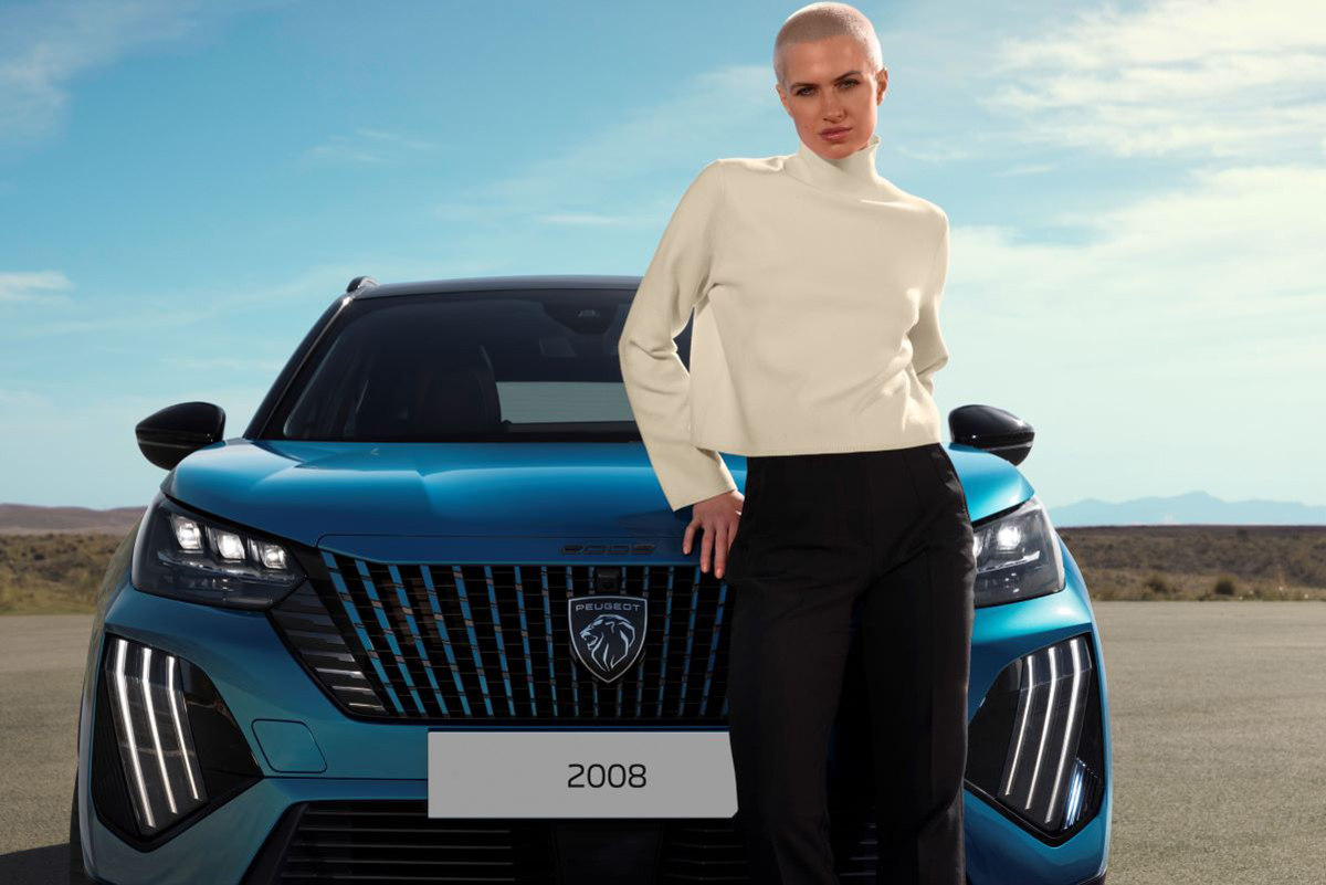 Peugeot 2008 s řidičkou pózující před vozem na otevřené silnici