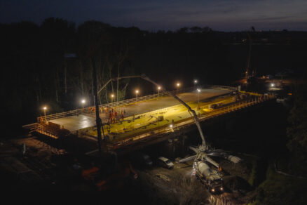 Pohled shora na noční betonáž mostu přes řeku Bystřici na úseku D35 Hořice–Sadová s osvětlenou pracovní plochou.