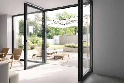 Otevřené velkoformátové balkonové dveře s úzkými okenními profily propojující interiér s terasou a zahradou