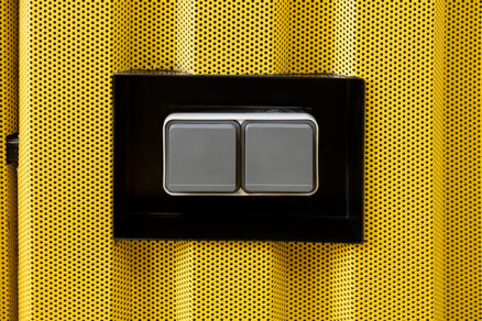 Moderní designový vypínač Hager v černém rámečku na perforovaném kovovém podkladu