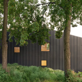 Moderní rodinný dům Black House v Praze s tmavou fasádou z titanzinku zasazený mezi vzrostlé stromy