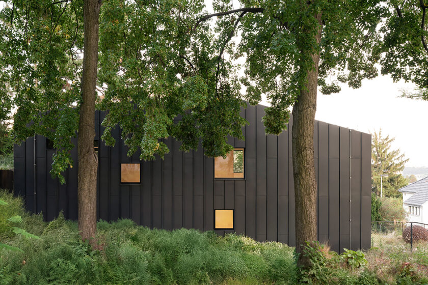 Moderní rodinný dům Black House v Praze s tmavou fasádou z titanzinku zasazený mezi vzrostlé stromy