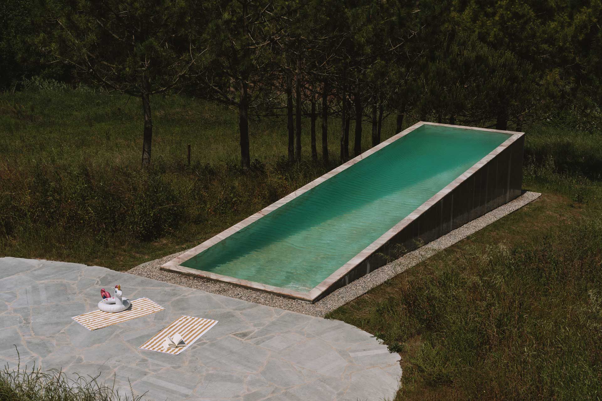 Podlouhlý bazén zasazený mezi stromy ve spodní části parcely sleduje přirozený sklon svahu.