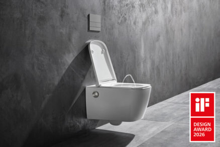 Závěsná sprchovací toaleta bez elektřiny při použití, proud vody z trysky, minimalistická koupelna s betonovou stěnou.