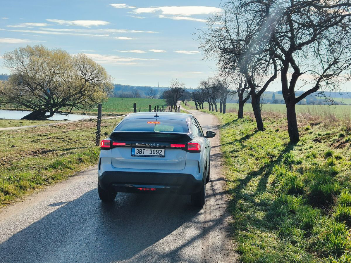 Citroën C4 jazdiaci po vidieckej ceste medzi stromami a lúkami