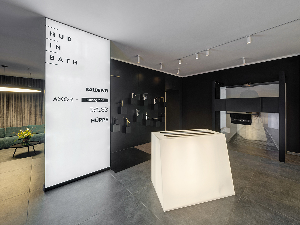 Moderní showroom koupelen v Karlíně s minimalistickým interiérem, tmavými stěnami a vystavenými bateriemi a sanitární technikou.