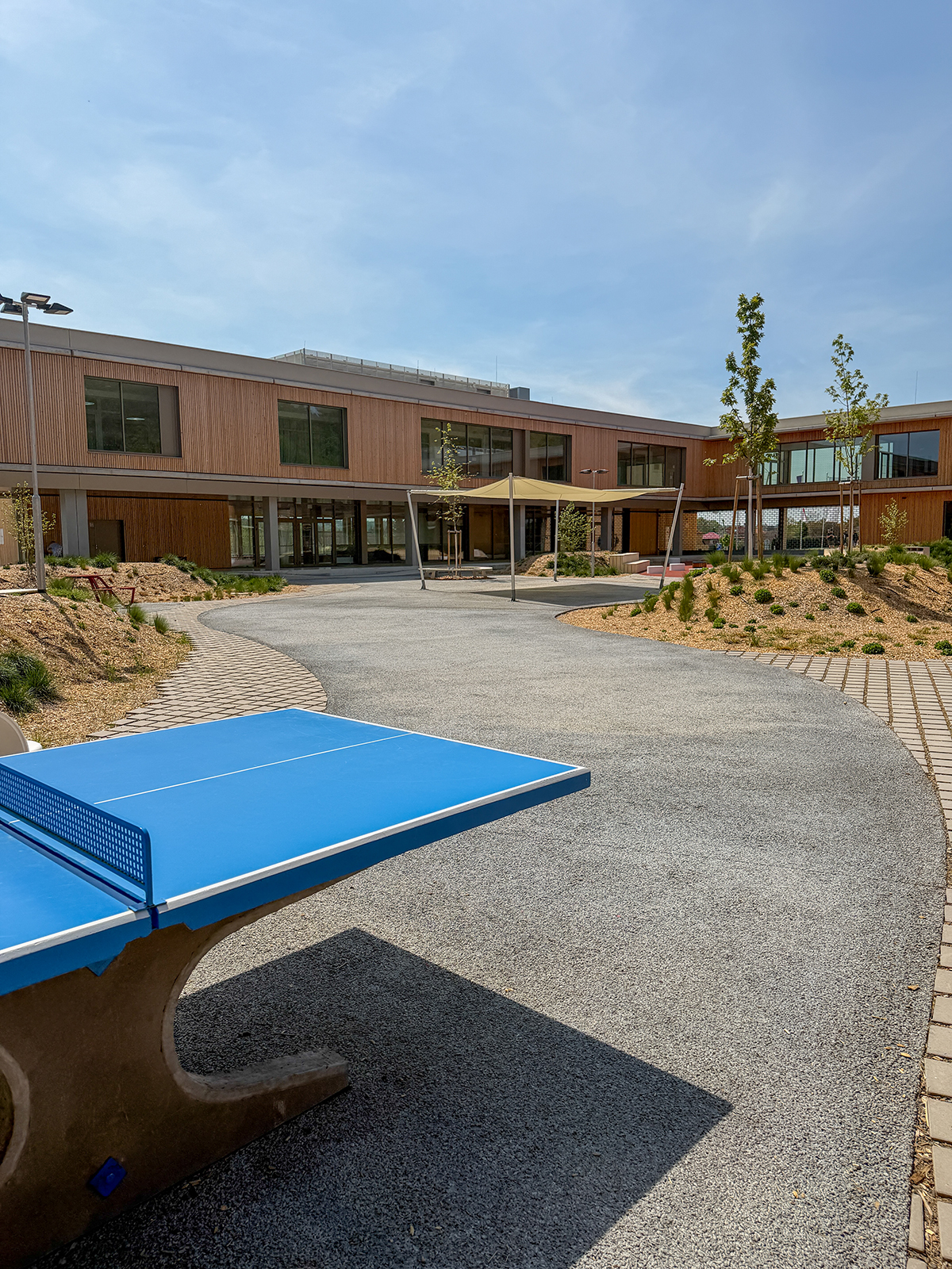Moderní školní dvůr s vodopropustným betonem a prvky pro venkovní výuku a odpočinek