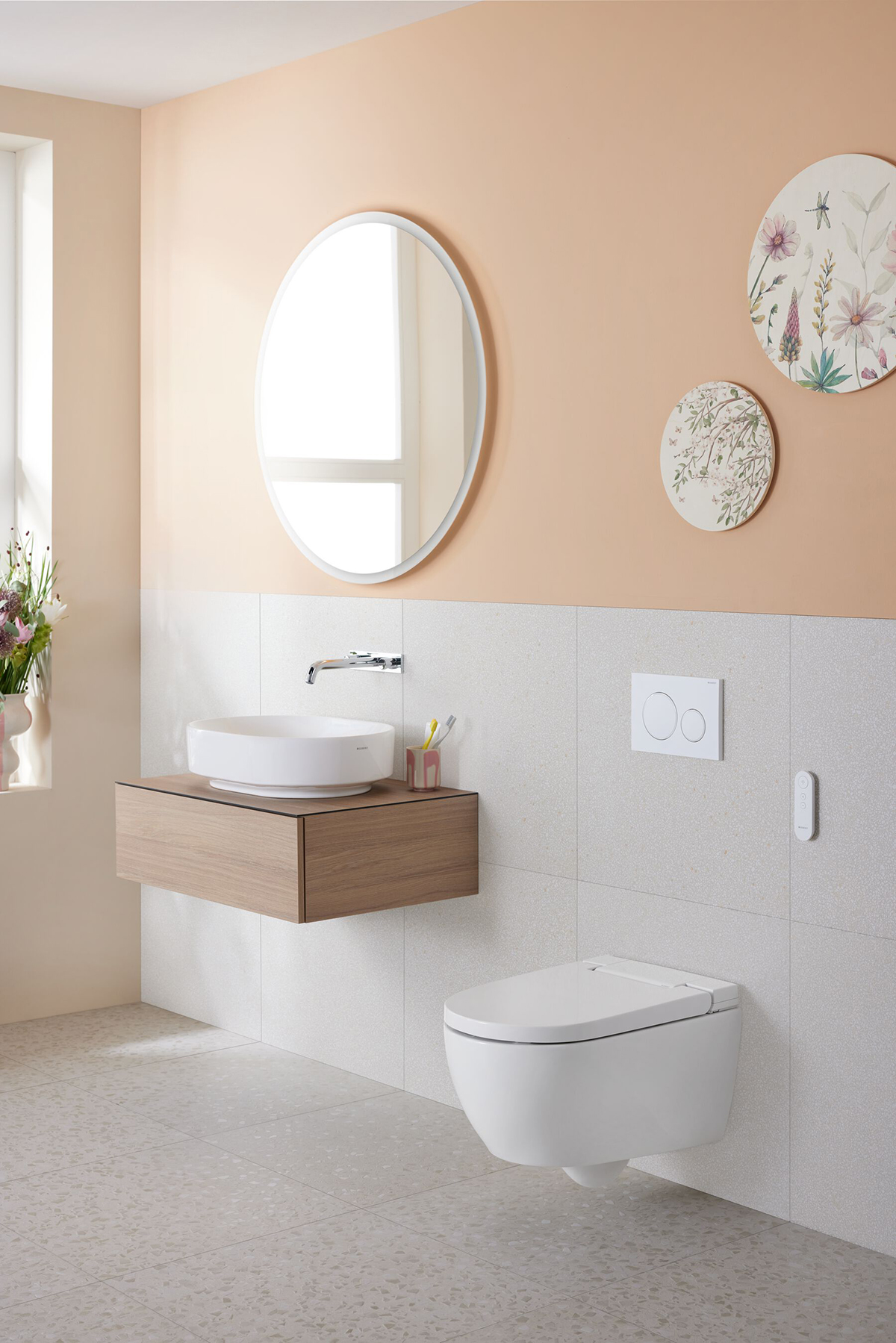 Sprchovací WC Geberit AquaClean Alba v koupelně s umyvadlem a kulatým zrcadlem