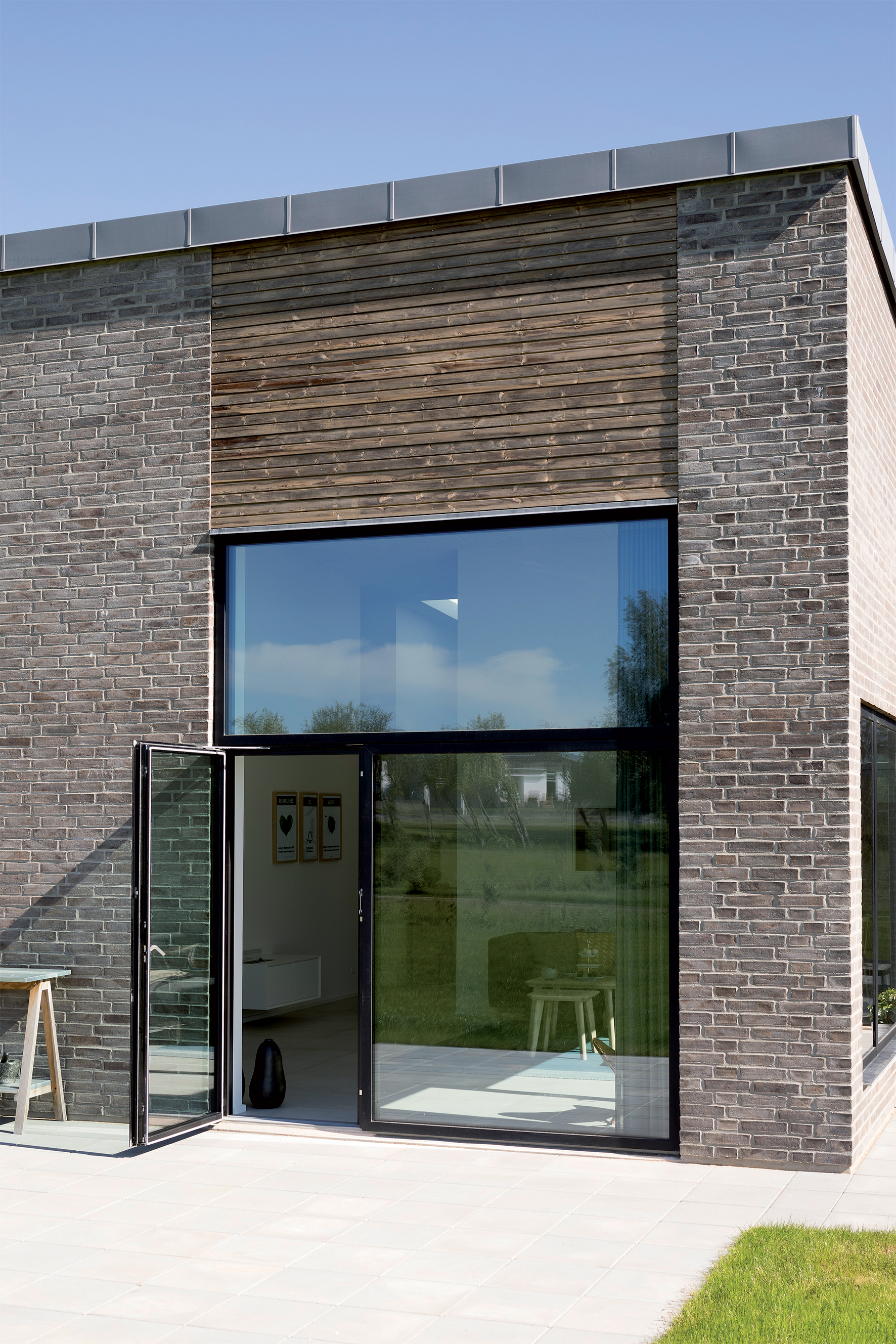 Fasáda zdůrazňuje texturu cihlové fasády v kontrastu s dřevěnými profily a černými rámy oken a dveří.