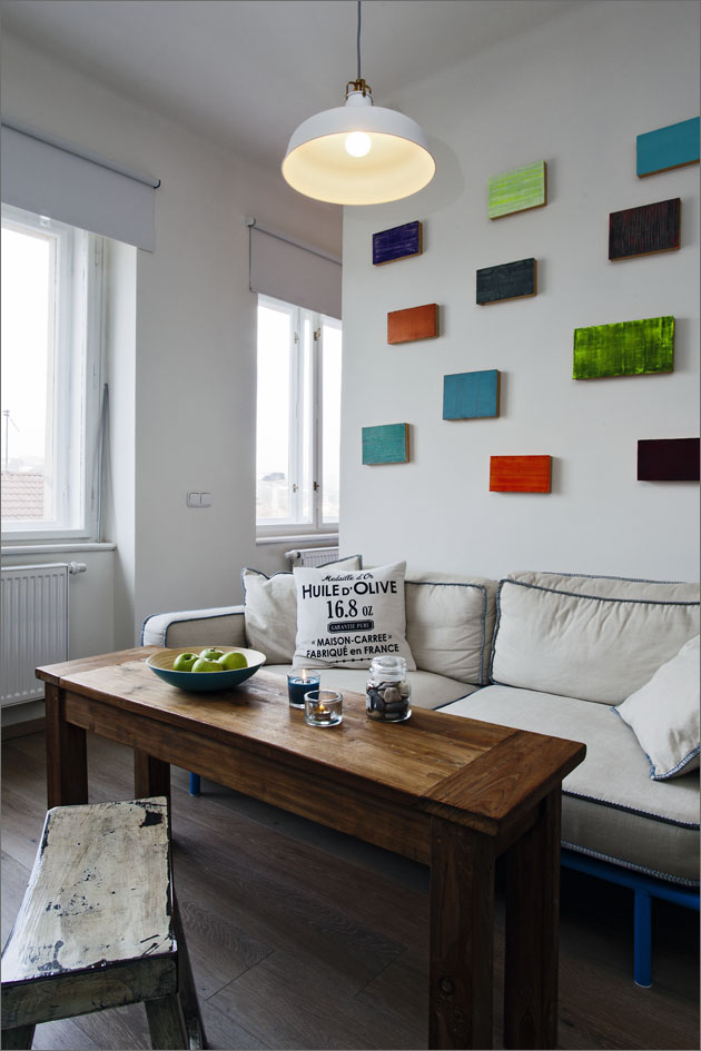 Na částečně otevřené stěně nad gaučem visí malé barevné panely v jasných barvách
