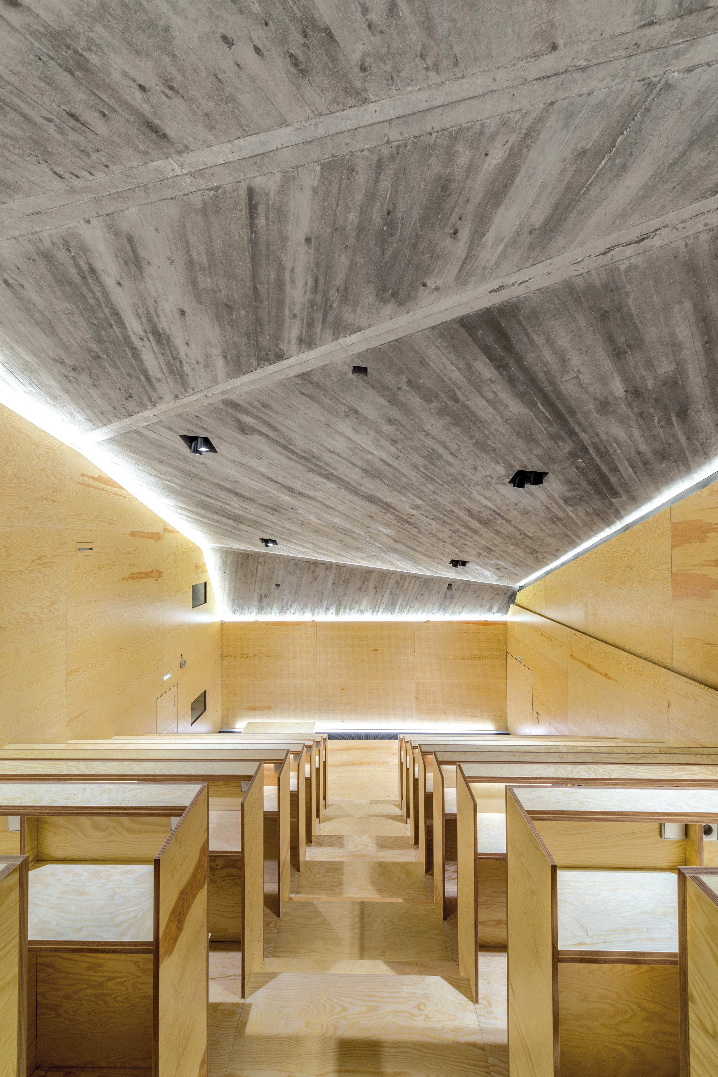 Interiér posluchárny a promítacího sálu je navržen z překližkových desek. Strop z pohledového betonu symbolizuje skálu.