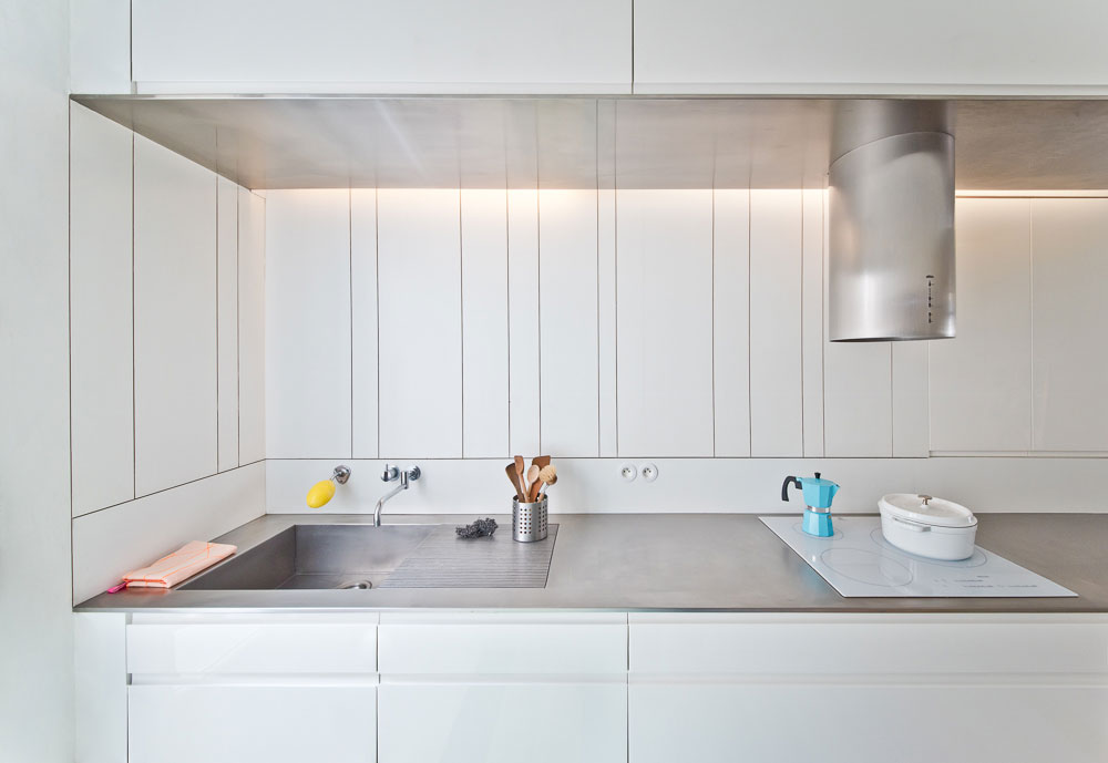 Hladké bílé plochy stěn i vybavení, které malý prostor prosvětlují a zvětšují, jsou použity také v kuchyni.