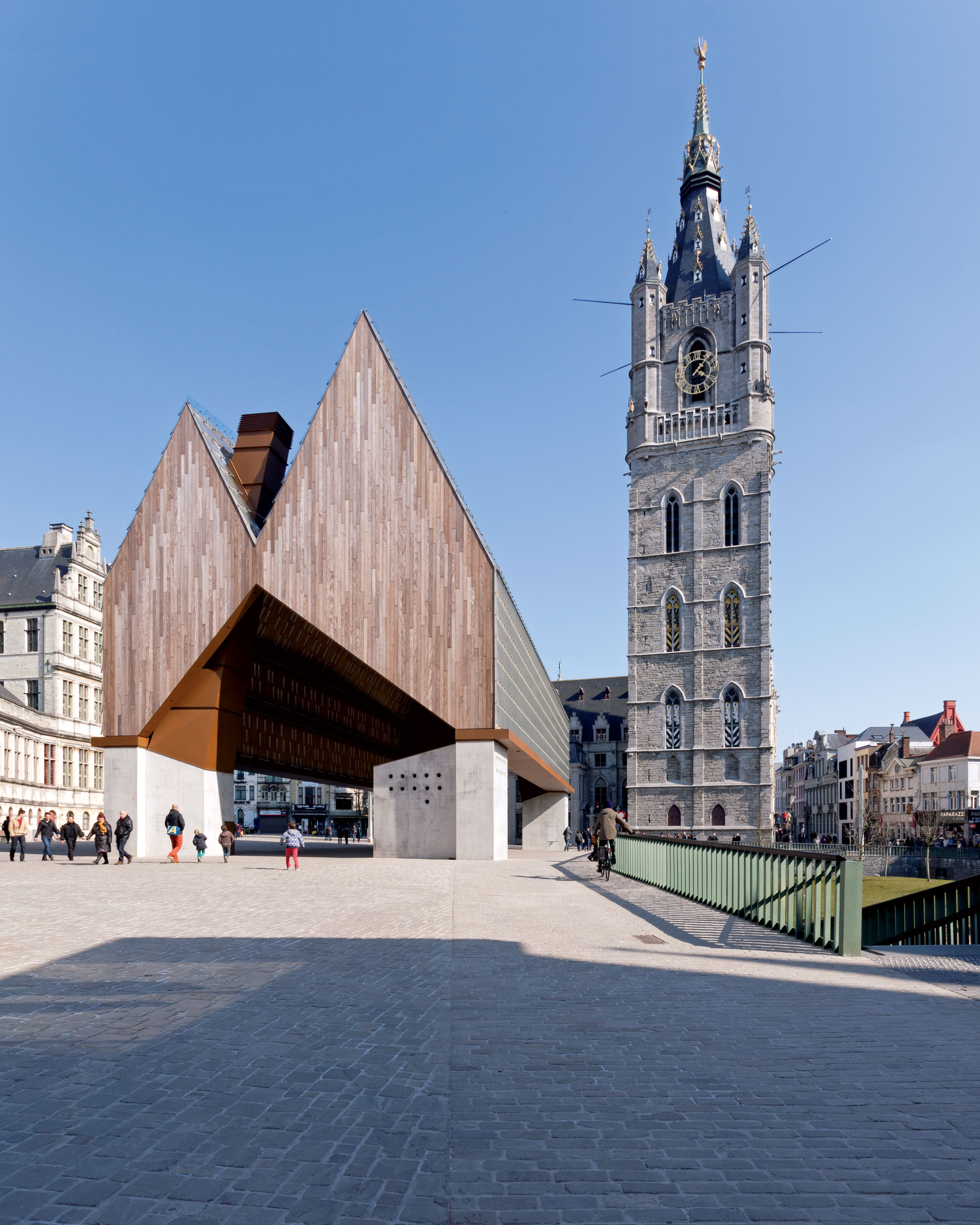 Současná architektura v prostředí historického dědictví Důležitým úkolem bylo novou tržnici o rozměrech 15,75 x 40 metrů integrovat do stávající zástavby města. Architekti se inspirovali klasickým bazilikálním prostorovým rozvrhem, jehož znaky našli v okolních chrámech sv. Mikuláše a sv. Bava. Překrytý veřejný prostor tržnice sestávající ze střechy nesené čtyřmi pilíři zcela osvobodili od stěn, otvorů a vstupů, aby docílili volnost pohybu, veřejnou interakci a adaptabilitu. Forma klasického svatostánku na čtyřech podporách je přitom inspirovala již od počátku projektu. Dramatická střešní krajina odkazuje na protější budovu radnice, ze které je profil střechy matematicky odvozený. Podélný sklon obou střešních sedel byl ve finální fázi návrhu posazený do opačných pozic, čímž se plasticita celé kompozice ještě více podpořila. Svými proporcemi a také výškou se stavba přizpůsobuje spíše nižší zástavbě náměstí.