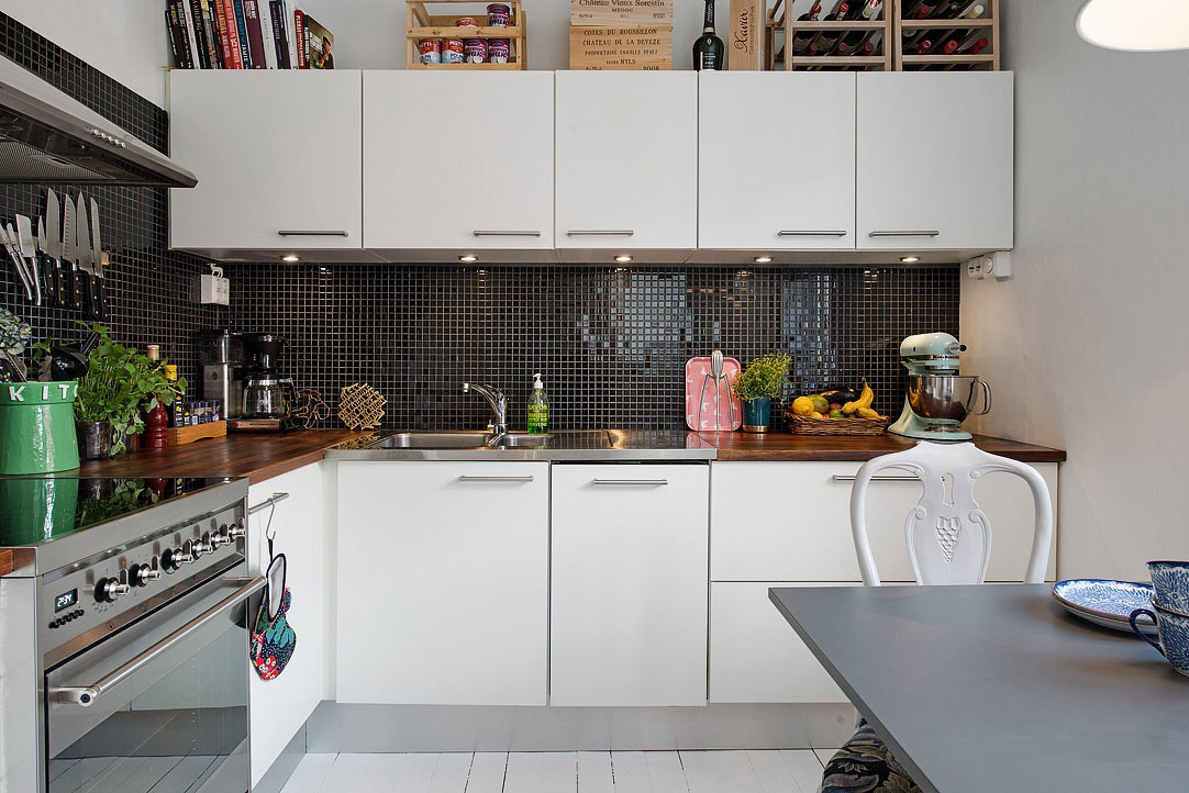 Velkorysý prostor umožňuje realizovat se v kuchyni několika kuchařům současně. Kontrast bílé linky a černé mozaikové zástěny krásně vertikálně odděluje jednotlivé roviny prostoru.