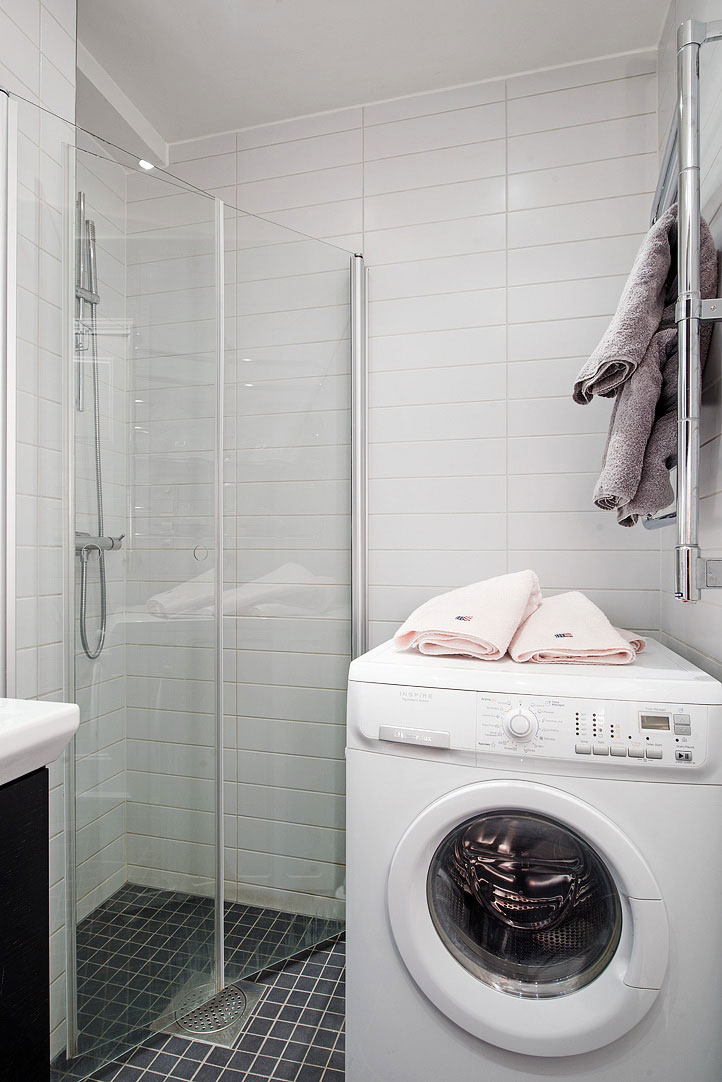 Kombinovaná pračka se sušičkou stojí vedle proskleného sprchového kouta.