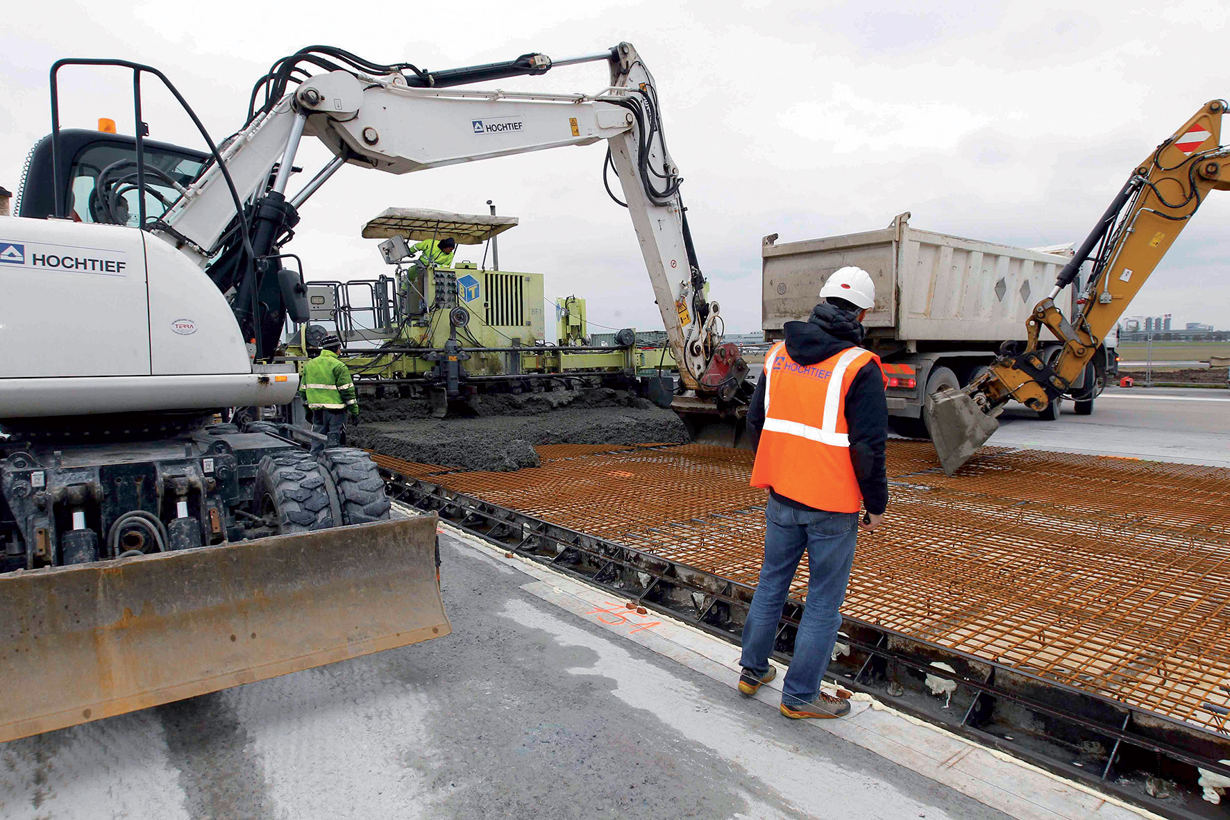 Vybírání betonu z nákladních aut pomocí dvojice bagrů