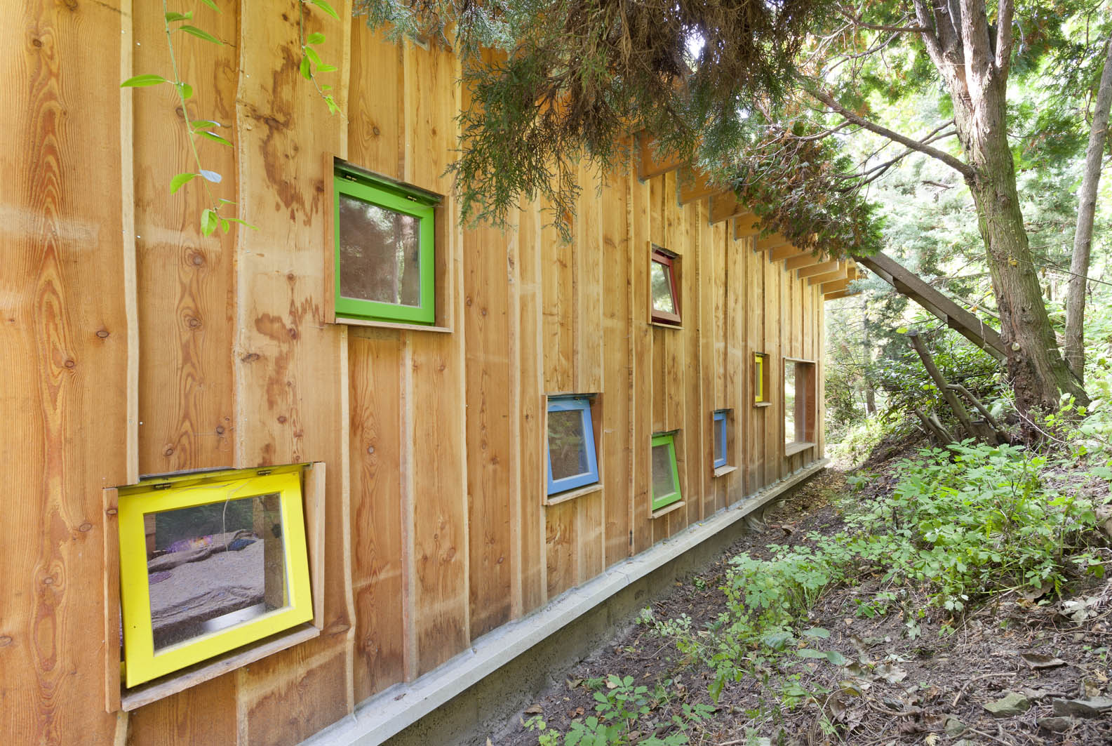 Zadní stěna chaty je dynamická a veselá – cikcak posetá barevnými větracími okénky osazenými v nestejné výšce.